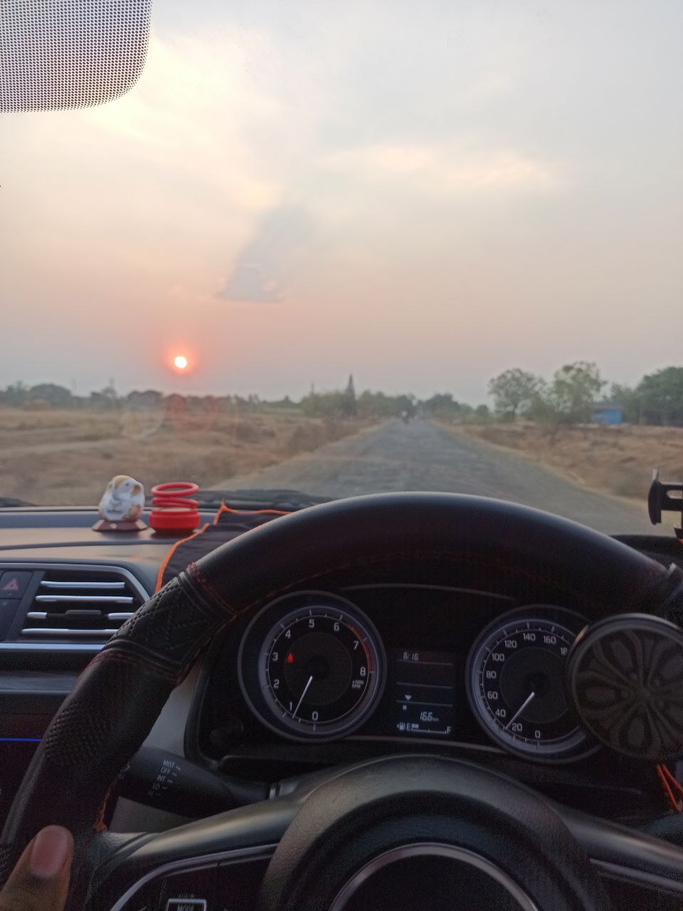 a view of a sunset through the steering wheel of a car
